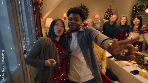 Asian woman with selfie stick records video or takes photos with family. Multi cultural family celebrating Christmas or New Year. Atmosphere of family Christmas dinner at home. Camera view.
