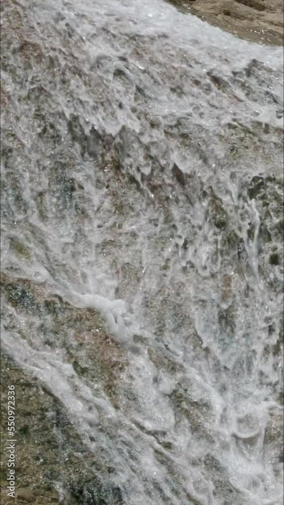 Slow panning shot of water cascading down the surface of a big rock in a waterfall Slow panning shot of water cascading down the surface of a big rock in a waterfall