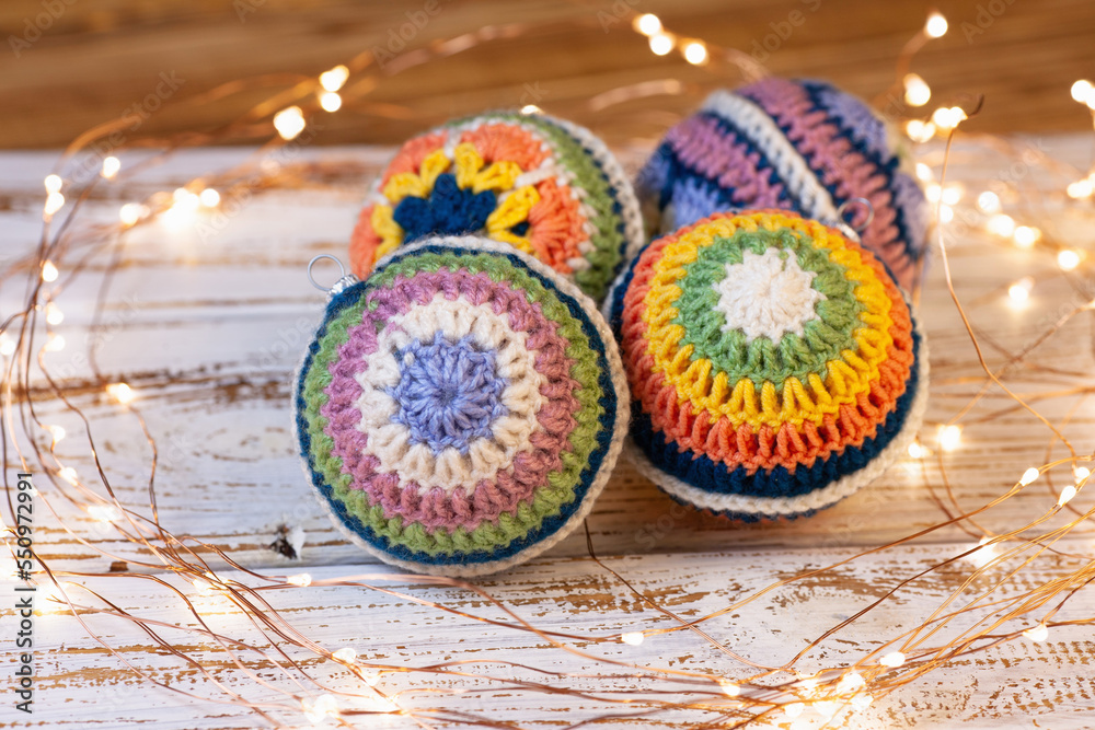 crocheted decorations for the Christmas tree. Bright balls with different crochet pattern of colored lace. White wooden background and led lights