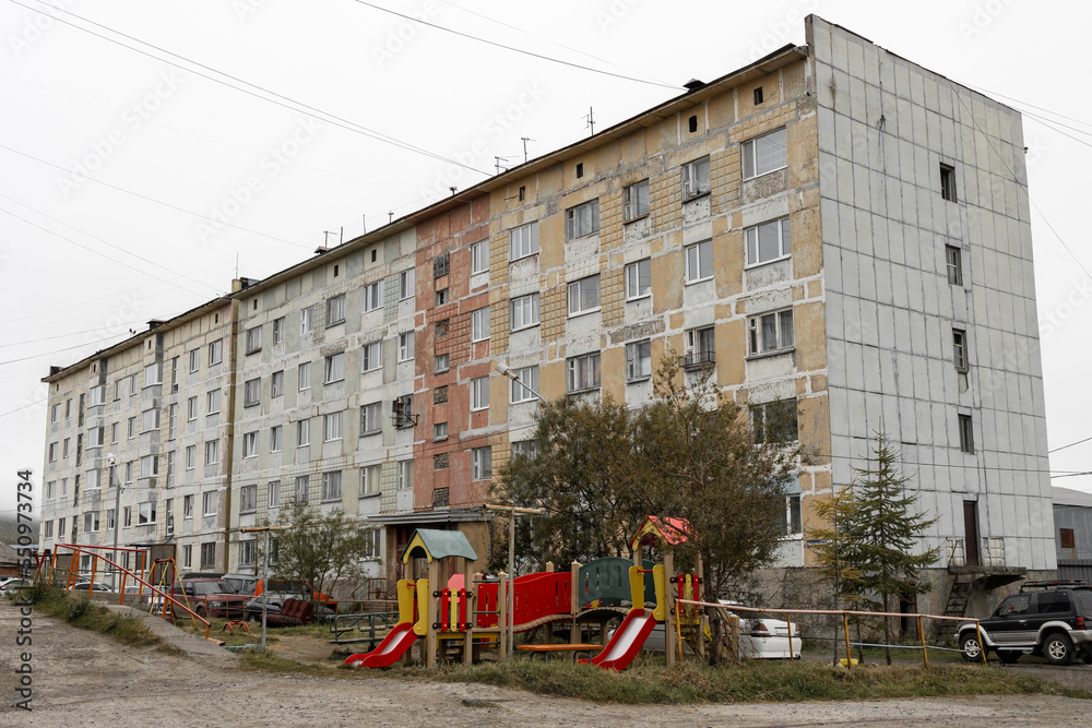 Fototapeta premium Children's playground in the city yard near the old panel building. Shabby wall of the house. Problems of improvement of old urban quarters in the province.