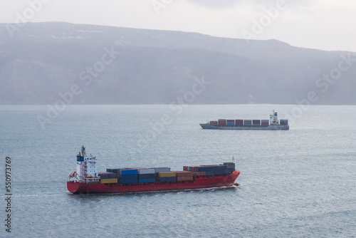 View of cargo ships sailing in the sea bay. Autumn seascape. Sea freight, logistics and supply in the Russian Far East. Container ships in Nagaev Bay, Sea of Okhotsk. Magadan, Magadan Region, Russia.