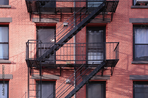 Close up New York City apartment building painted red brick exterior, windows, and diagonal fire escape stairs