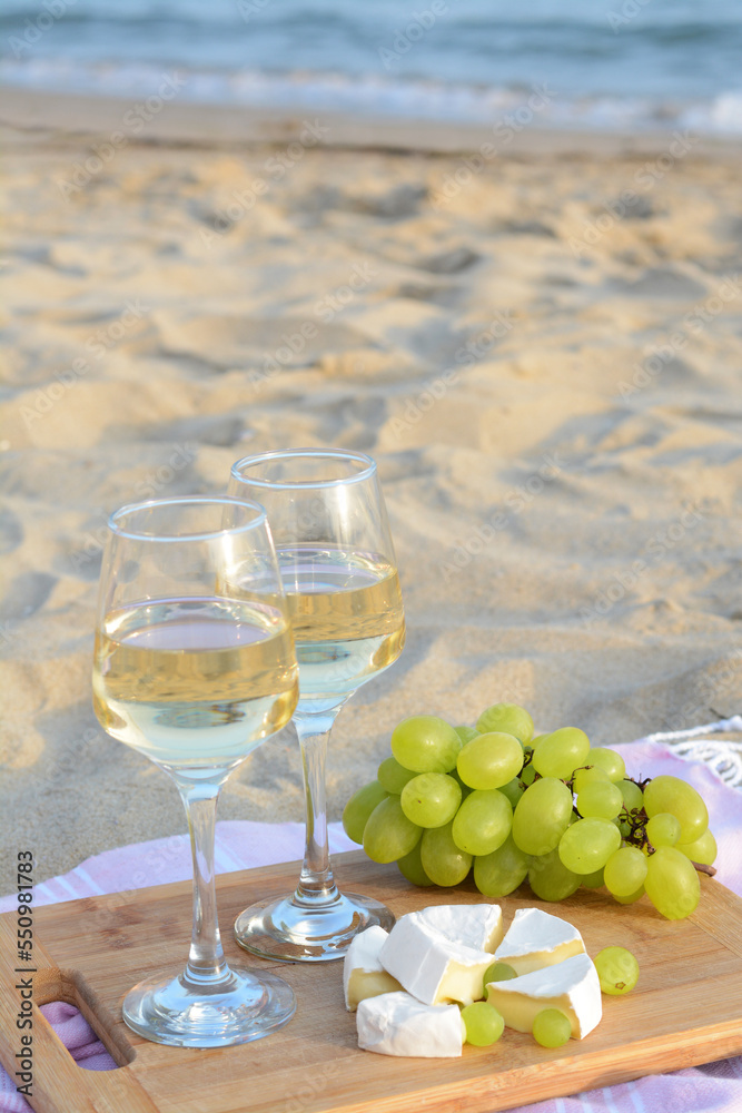 Fototapeta premium Glasses with white wine and snacks for beach picnic on sandy seashore