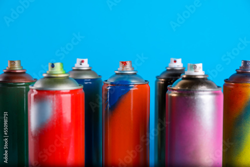 Used cans of spray paints on light blue background, closeup