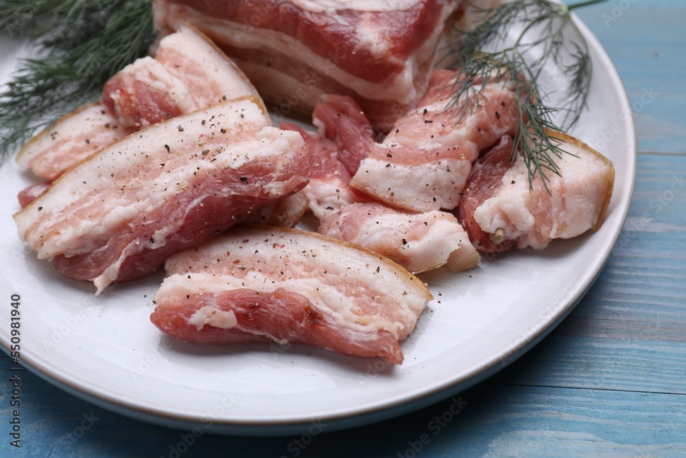 Pieces of pork fatback with dill on light blue wooden table, closeup
