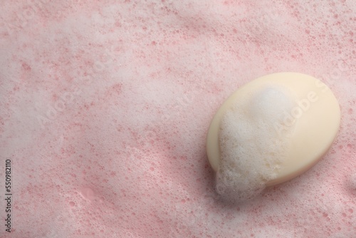 Soap with fluffy foam on pink background, top view. Space for text