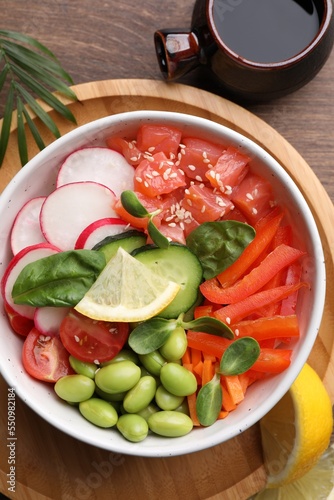 Poke bowl with salmon  edamame beans and vegetables on wooden table  flat lay
