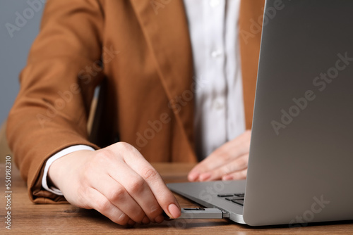 Woman attaching usb flash drive into laptop at wooden table, closeup photo