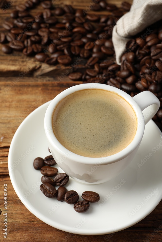Cup of hot aromatic coffee and roasted beans on wooden table Cup of hot aromatic coffee and roasted beans on wooden table