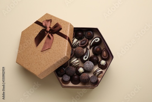 Open box of delicious chocolate candies on beige background, top view