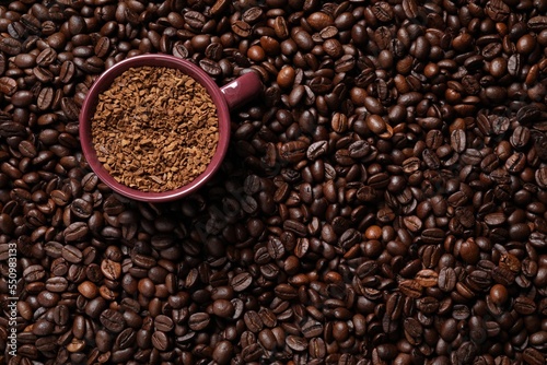 Cup with instant coffee on roasted beans, top view. Space for text