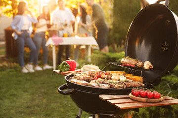 Group of friends having party outdoors. Focus on barbecue grill with food. Space for text