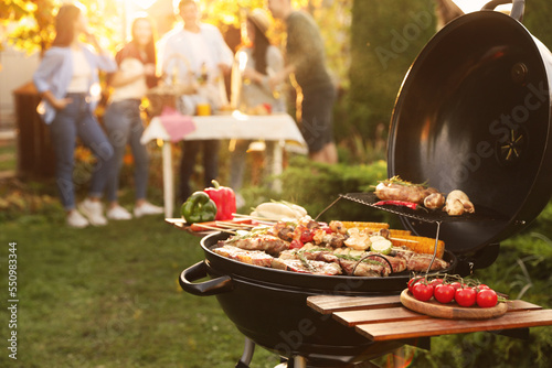 Group of friends having party outdoors. Focus on barbecue grill with food. Space for text photo