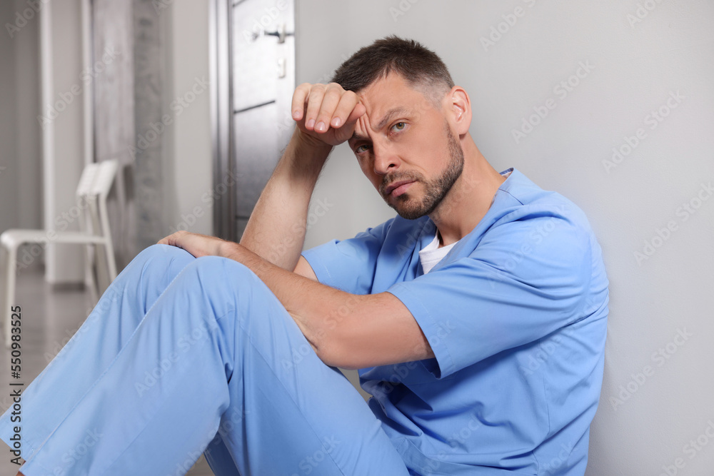 Exhausted doctor near grey wall in hospital corridor Exhausted doctor near grey wall in hospital corridor