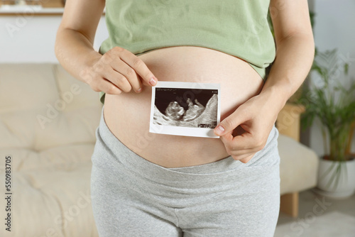 Pregnant woman with ultrasound picture of baby in living room, closeup