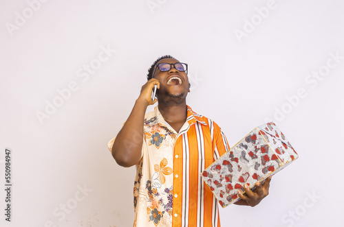 Happy young African american male wearing glasses holding a gift box and making a phone call