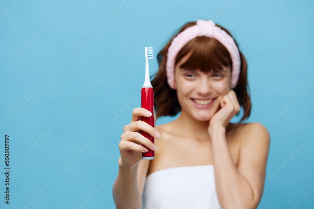 woman is standing in a white towel facing the camera, holding a red toothbrush in her hand and holding it out to the viewer, smiling broadly with even, light teeth and holding her hand on her cheek woman is standing in a white towel facing the camera, holding a red toothbrush in her hand and holding it out to the viewer, smiling broadly with even, light teeth and holding her hand on her cheek