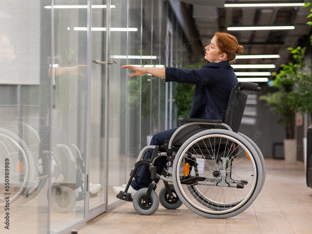 Obraz premium Red-haired caucasian woman in a wheelchair trying to open the door in the office. 