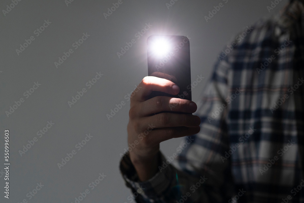 hand holding a smartphone used as a torched, flashlight of mobile phone in the dark - obrazy, fototapety, plakaty 