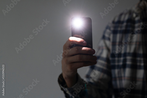 hand holding a smartphone used as a torched, flashlight of mobile phone in the dark