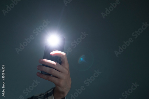 hand holding a smartphone used as a torched, flashlight of mobile phone in the dark