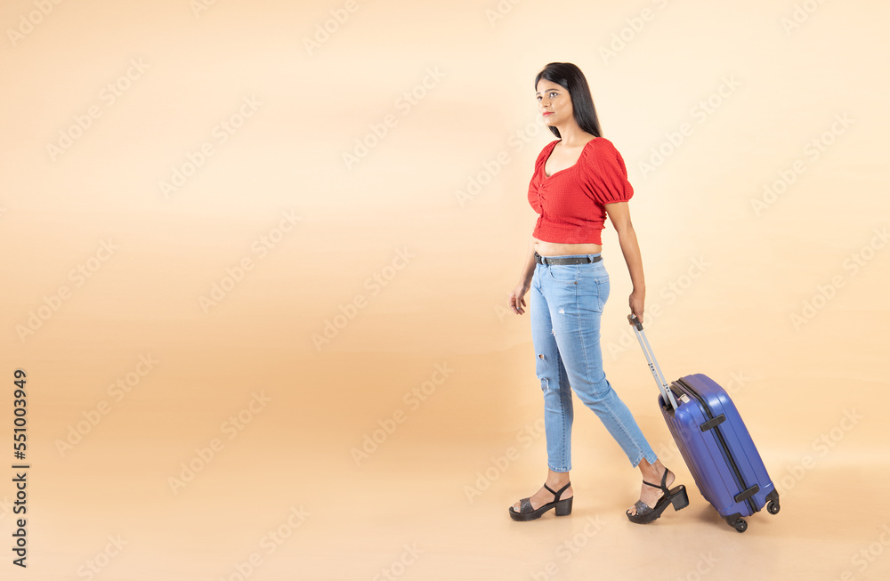 Young Indian Asian woman wearing casual being ready to go on vacation traveling trip with travel trolly bag luggage isolated over beige background, Studio shot,. People lifestyle, copy space.