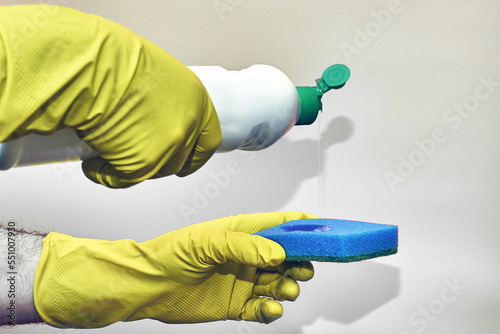 a man in rubber household gloves pours detergent from a bottle onto a sponge on a light background