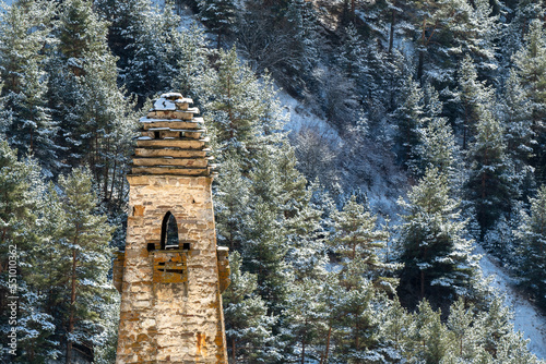 Old Ingush tower against snowy mountain forest on sunny winter day. Niy, Ingushetia, Caucasus, Russia. photo