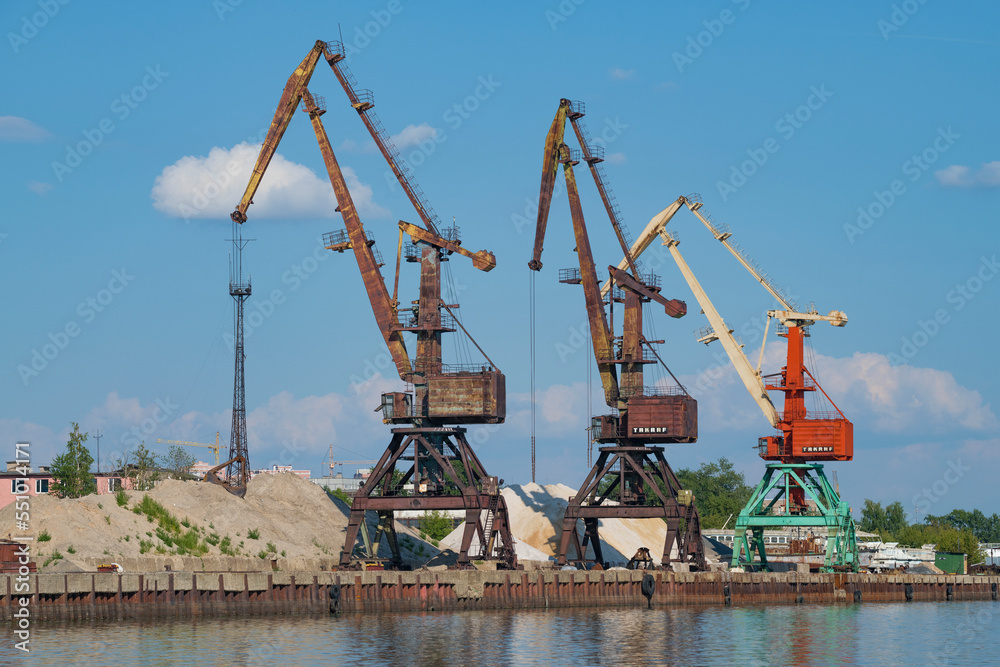 Three port cranes in the river port on a sunny summer day