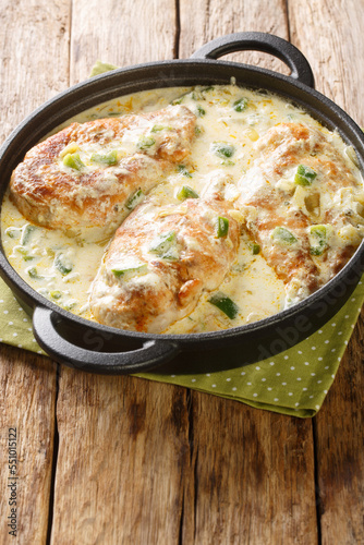 Pollo con crema features a delicious combo of tender chicken simmered in a Mexican style creamy sauce closeup in the pan on the wooden table. Vertical