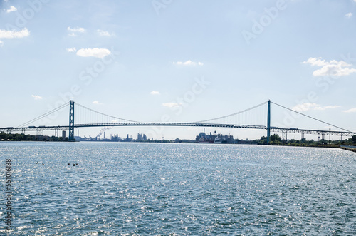 The Ambassador Bridge connects Detroit, Michigan, and Windsor Ontario over the Detroit river.  Taken from West Riverfront Park in the daytime on a mostly clear day. Waves can be seen in the river.. photo