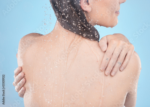 Back, woman and shower for skincare, clean and hygiene against blue studio background. Young female, girl and liquid drops for washing, body care or natural beauty for wellness, water splash or relax