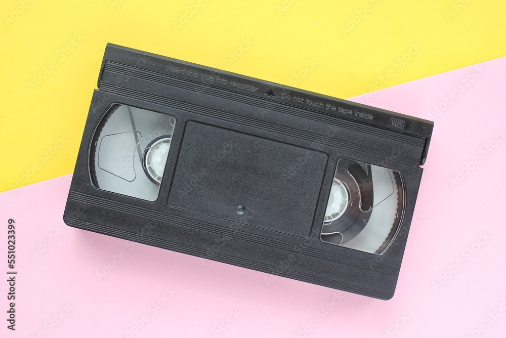 Black VHS videotape cassette on yellow and pink background. Old obsolete technology for tape recording and watching media movies. Retro, vintage, history, nostalgia concept. Top view, flat lay