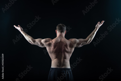 muscular bodybuilder in black studio. strong bodybuilder has muscular back muscles.