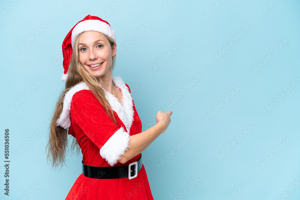 Young blonde woman dressed as mama claus isolated on blue background pointing back Young blonde woman dressed as mama claus isolated on blue background pointing back