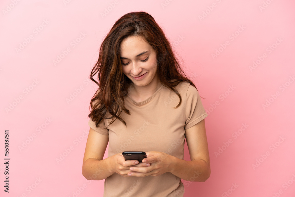 Young caucasian woman isolated on pink background sending a message with the mobile Young caucasian woman isolated on pink background sending a message with the mobile