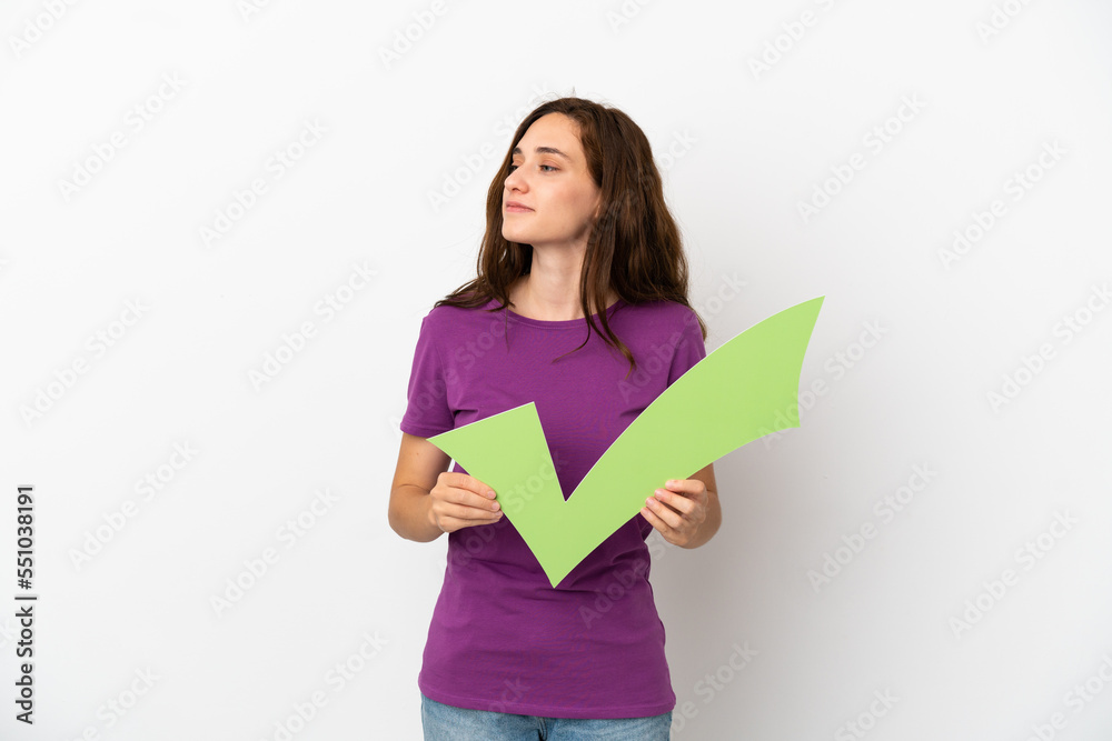 Young caucasian woman isolated on white background holding a check icon and looking side Young caucasian woman isolated on white background holding a check icon and looking side