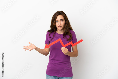 Young caucasian woman isolated on white background holding a downward arrow and with sad expression