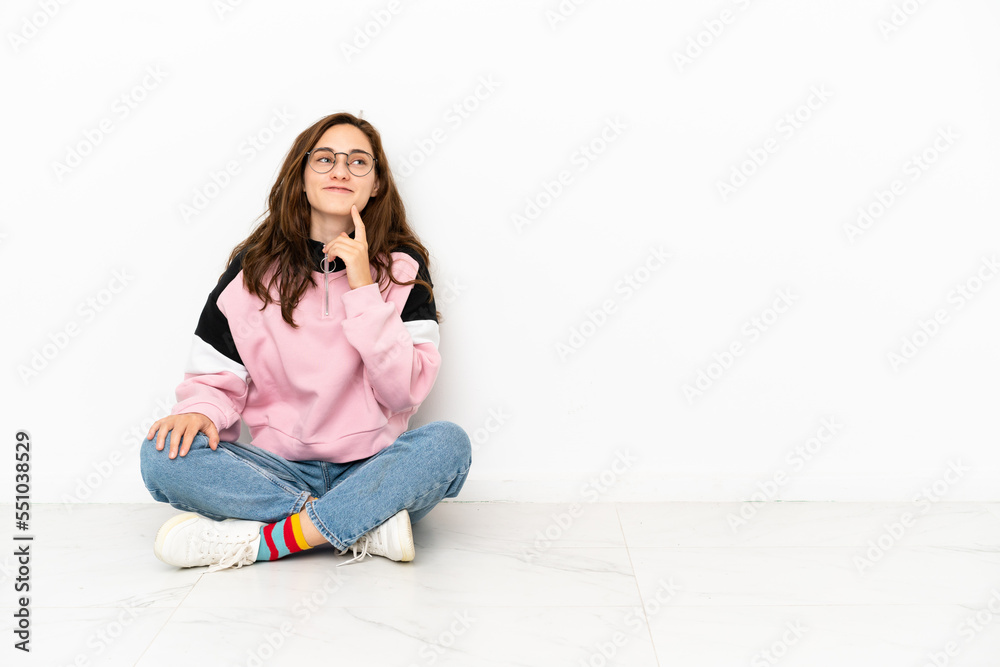 Young caucasian woman sitting on the floor isolated on white background thinking an idea while looking up Young caucasian woman sitting on the floor isolated on white background thinking an idea while looking up