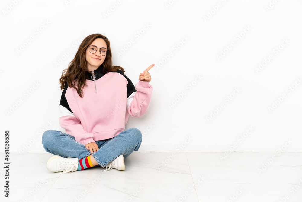 Young caucasian woman sitting on the floor isolated on white background pointing finger to the side Young caucasian woman sitting on the floor isolated on white background pointing finger to the side
