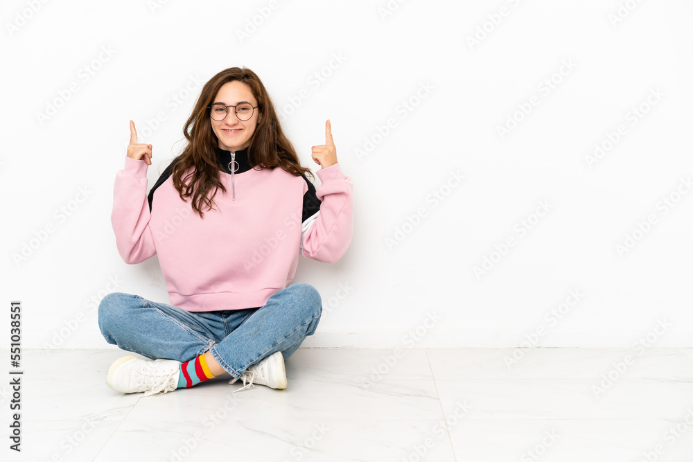 Young caucasian woman sitting on the floor isolated on white background pointing up a great idea