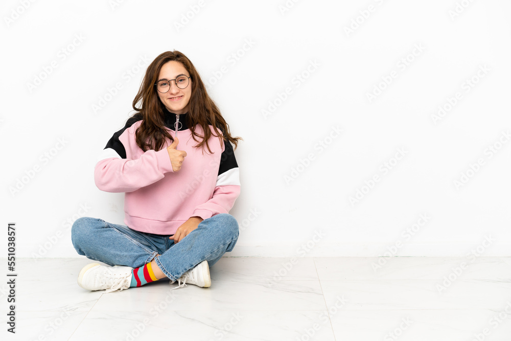 Young caucasian woman sitting on the floor isolated on white background giving a thumbs up gesture Young caucasian woman sitting on the floor isolated on white background giving a thumbs up gesture