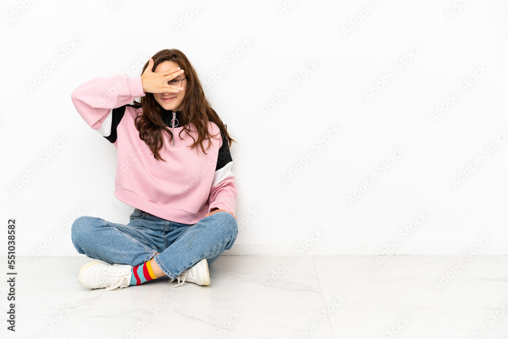 Young caucasian woman sitting on the floor isolated on white background covering eyes by hands and smiling Young caucasian woman sitting on the floor isolated on white background covering eyes by hands and smiling