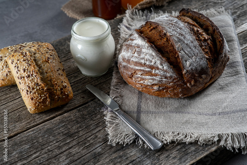 Bread, croissants, rolls, homemade yogurt, marmalade and honey jars, oranges, apples and sliced ​​grapefruit on the table in a rustic wooden bowl and wooden plate, with wooden boards background