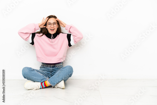 Young caucasian woman sitting on the floor isolated on white background with surprise expression