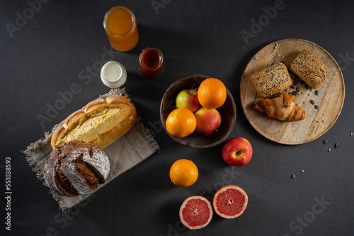 Bread, croissants, rolls, homemade yogurt, marmalade and honey jars, oranges, apples and sliced ​​grapefruit on the table in a rustic wooden bowl and wooden plate