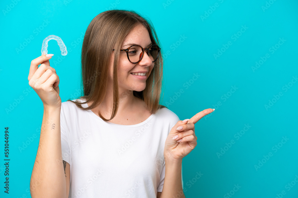 Young Lithuanian woman holding invisible braces isolated on blue background pointing to the side to present a product