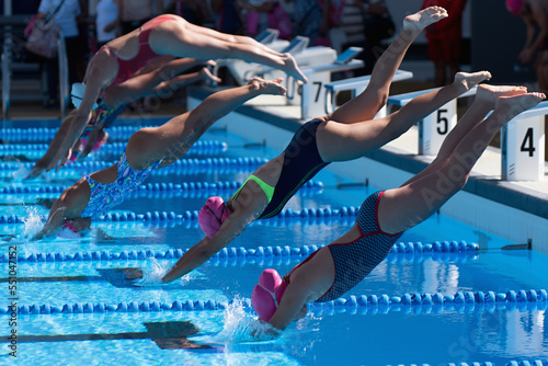 Female swimmers dive off the platform into the swimming pool to swim race photo