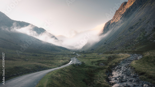 Clouds roll over Honister Pass after sunrise. Beautiful landscape scenery in Lake District, UK. Cloud inversion in a mountain valley with a road and stream. photo