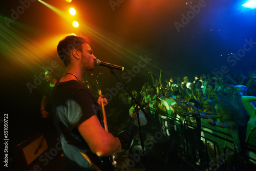 Concert, band and music with a man guitarist playing at a gig for a crowd or audience at a performance event. Festival, stage and social with a male artist strumming a guitar while singing at a show